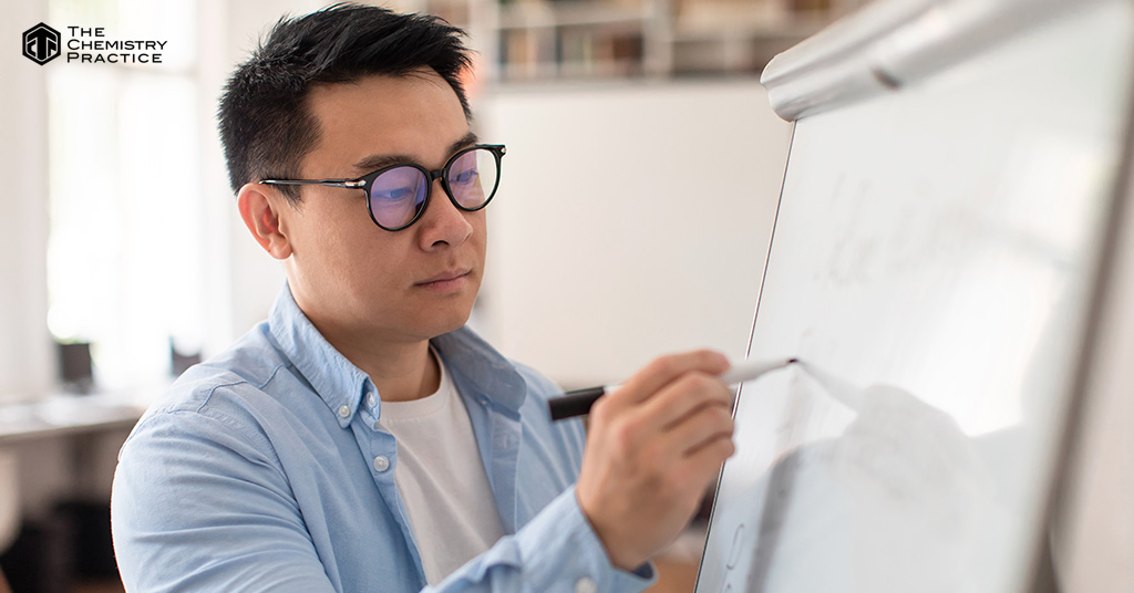 Asian Professor giving lecture writing on whiteboard in classroom