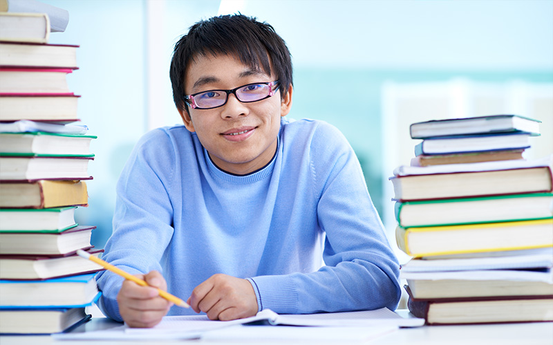 Smiling student sitting at desk between stacks of chemistry textbooks.